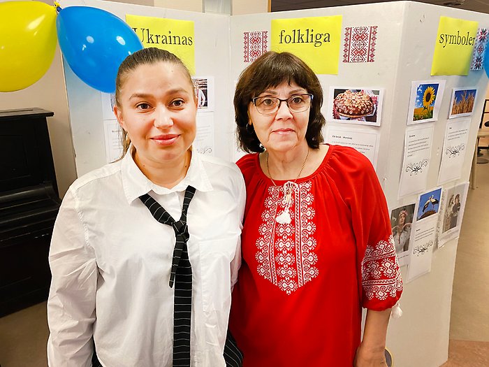 Två kvinnor ler och tittar in i kameran. I bakgrunden syns en gul och en blå ballong och bilder från Ukraina.