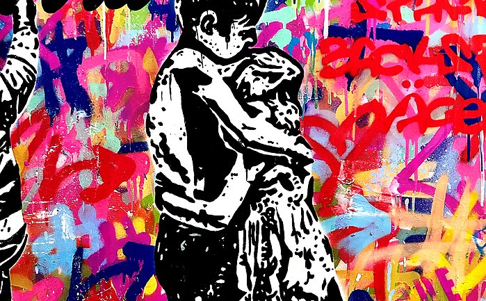 En flicka och en pojke som kramas framför en vägg med massor av klotter på